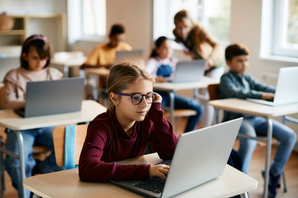 A junior high student with a female gender expression using a laptop in a classroom.